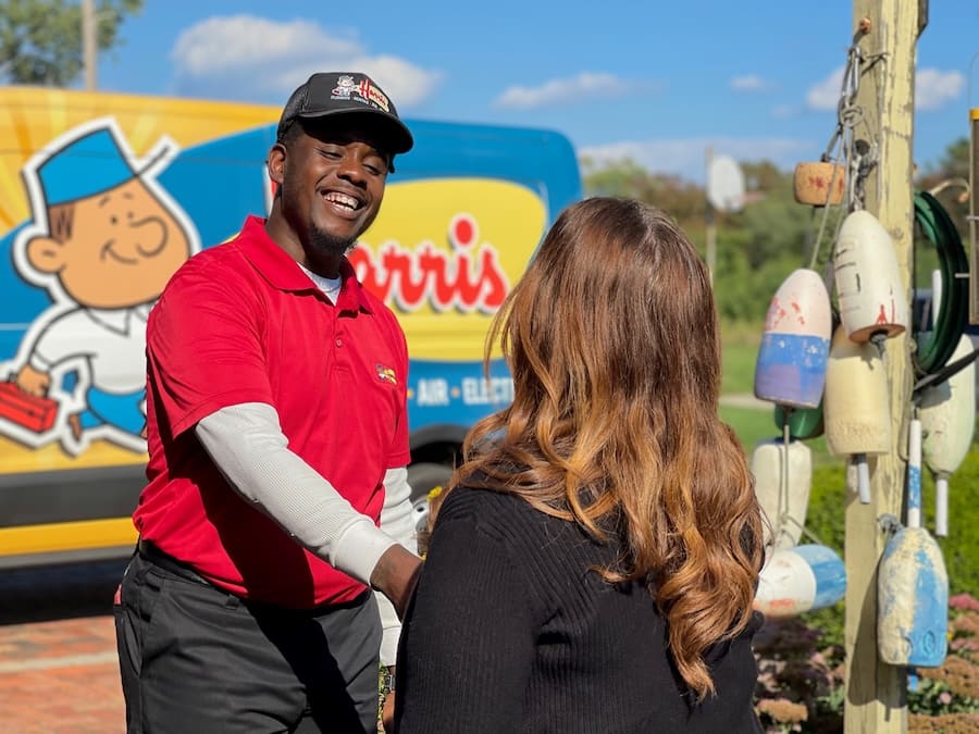 Delivery worker in a red polo shakes hands with a woman outdoors, smiling, with a cartoon van in the background.