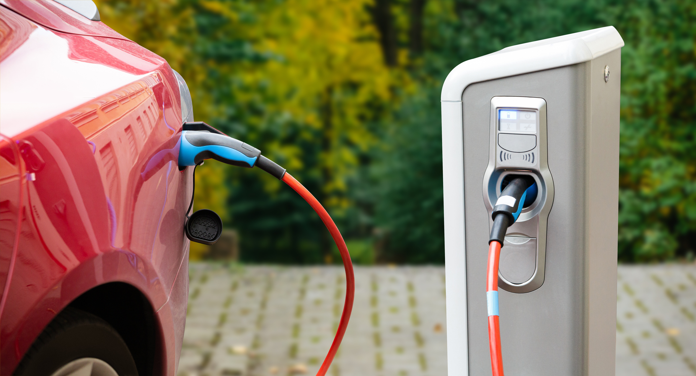 Close up of home electric vehicle charger plugged into red car