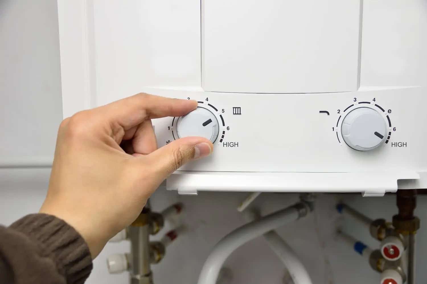 A close-up of a hand adjusting the setting on a tankless water heater. 