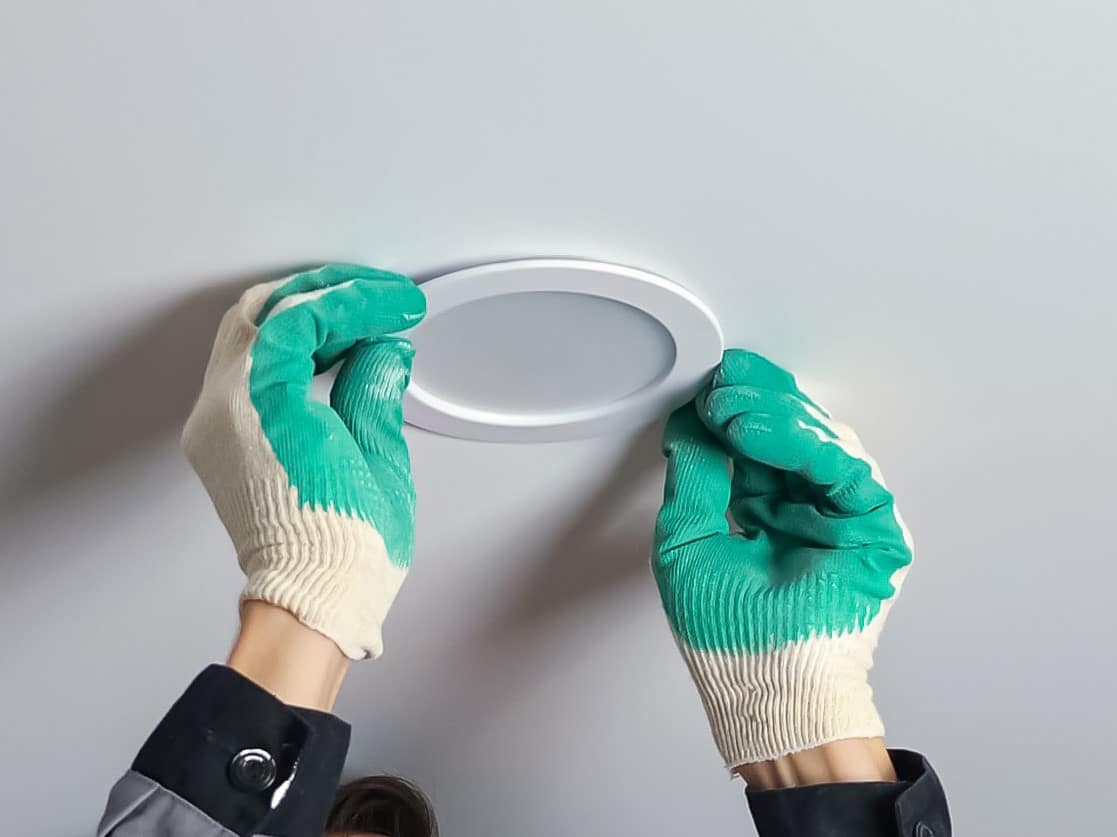 Electrician installs light on ceiling at flat renovation