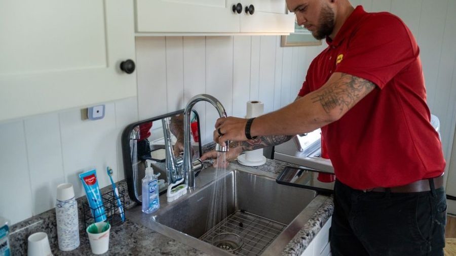 Plumber performing professional leak detection under a kitchen sink, inspecting plumbing connections and fixtures to identify hidden water leaks.