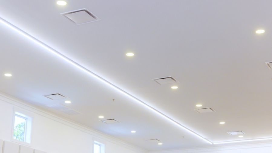 Modern white ceiling with recessed LED lighting, linear cove lighting, and multiple air vents in a clean commercial interior.